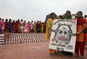 Activists of “Daughters of Freedom Fighters” stand with a caricature of a war criminal to demand punishment, as others stand in a queue to pay tribute at the memorial for war heroes to mark the country’s Independence Day, in Saver, on the outskirts of Dhaka, Bangladesh, Friday, March 26, 2010.  The poster translates to “We demand punishment for war criminals. They are a disgrace.” (AP Photo/Pavel Rahman)